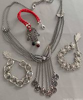 Lot overview showing necklace, red cord bracelet, two silver-tone bracelets