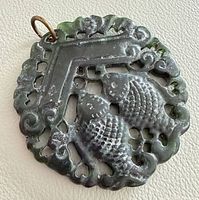Front view of round dark green jade pendant with double fish carving and metal loop