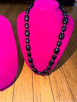 Full view of black oval bead necklace displayed on stand