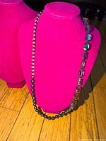 Full view of necklace on magenta display bust showing bead sections