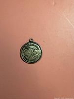 Front view of round sterling silver pendant charm with Strickland’s Mt. Inn Mount Pocono inscription and double-heart motif