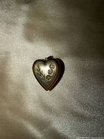 Front of heart-shaped gold locket showing engraved leaf design and three inset diamonds