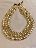 Full view of three-strand faux pearl necklace laid flat