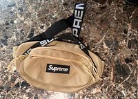 Front view showing tan body, Supreme logo patch, twin zippers, branded strap