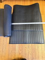 Rolled and flat black ribbed mat with measuring tape showing width