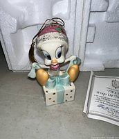 Front view of Tweety Bird porcelain ornament on gift box with hanging cord and hat