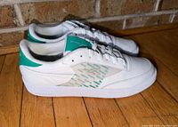Side view of both sneakers showing white leather uppers and green heel accents
