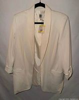 Front view of cream Anne Klein blazer on hanger showing shawl collar, 3/4 sleeves, welt pockets, tag attached.