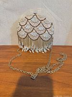 Front view of champagne satin hard-case clutch showing bead scallop design, fringe tassels and gold chain