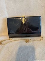 Front view of black patent leather Farnell clutch with gold-tone kiss-lock clasp and chain strap displayed