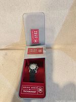 Watch in open tin showing dial, strap and interior branding