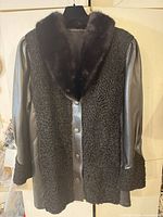 Front view of black astrakhan coat showing leather sleeves, fur collar, snap closures