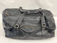 Top view of black leather tote bag, handles snapped together, front zipper pocket visible