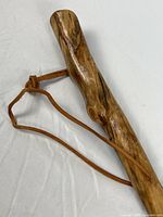 Upper section of wooden walking stick showing polished grain and attached leather wrist strap