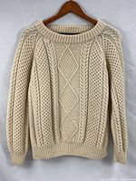 Front view of cream wool Aran sweater on hanger