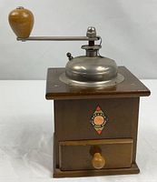 front view of wooden coffee grinder showing label, drawer, crank and hopper