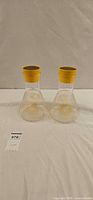 two Pyrex glass beaker carafes with yellow lids on white background