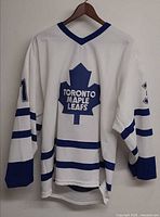Front view of white Toronto Maple Leafs jersey showing crest and sleeve numbers
