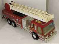 Left front perspective of red metal fire truck showing ladder extended and side decals
