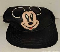 Front view of black faux-leather cap with Mickey Mouse face patch