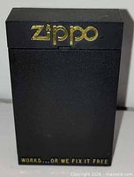 Front of closed black Zippo presentation box showing gold logo and slogan