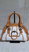 Front view of handbag showing white leather body, tan embossed trim, ring detail, double handles