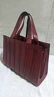 Front angle of maroon seamed leather tote with straps upright