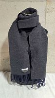 Scarf displayed grey side outward on mannequin, showing fringe and Sandro label