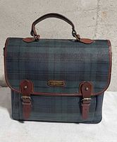 Front view showing Blackwatch plaid pattern, dual buckle straps, brand plaque
