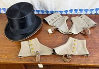 Overview of black top hat and four beige spats on wood surface