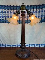 Full view of lamp illuminated showing wood column, brass arms, both glass shades, base, cord