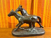 Front left view of bronze finish two-horse sculpture on oval base
