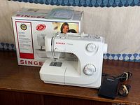 Singer sewing machine beside original box and foot pedal