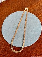 Full view of tri-tone braided necklace on blue felt