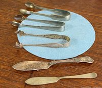 All items laid out: four sugar tongs, ornate knife, spreader