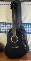 Full view of black Vangoa cutaway acoustic-electric guitar standing in front of included gig bag