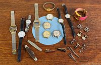 Overview of all watches, cufflinks, tie clips and knife on wooden surface