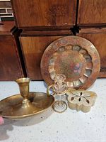 All four items grouped: brass candle holder, enameled plate, glass perfume bottle, inlaid stone box