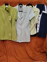 Four uniform tops hanging: green tunic, light blue jacket, pale aqua blouse, navy top with white collar