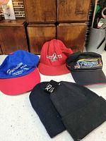 Group shot of all five hats on countertop: three baseball caps front row, two knit beanies front right