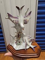 Front view showing two porcelain doves with purple accents on iridescent branch, wooden base visible