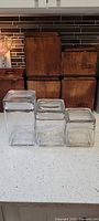 Front view of three graduated square glass jars with lids