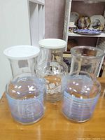 Group view of three glass pitchers showing two with blue stripes and lids, one with white floral design