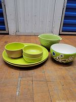 Group shot showing all seven green melamine pieces: two plates, three small bowls, two larger bowls