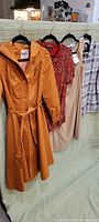 Four garments hanging: burnt-orange coat, red Cartise dress, beige dress, plaid shirt