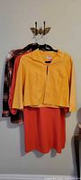 All three garments hanging: mustard jacket over orange dress with plaid shirt behind