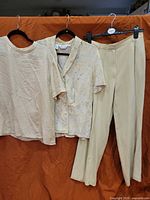Group shot of beige tee, floral Gillian blouse, and beige trousers hanging