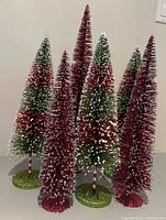 Front view of six red and green bottle brush trees with snow flecks and glitter bases
