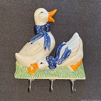 Front view showing ceramic ducks, blue bow, three metal hooks and mounting holes