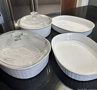 Group shot of four white CorningWare French White dishes, two round with lids and two oval